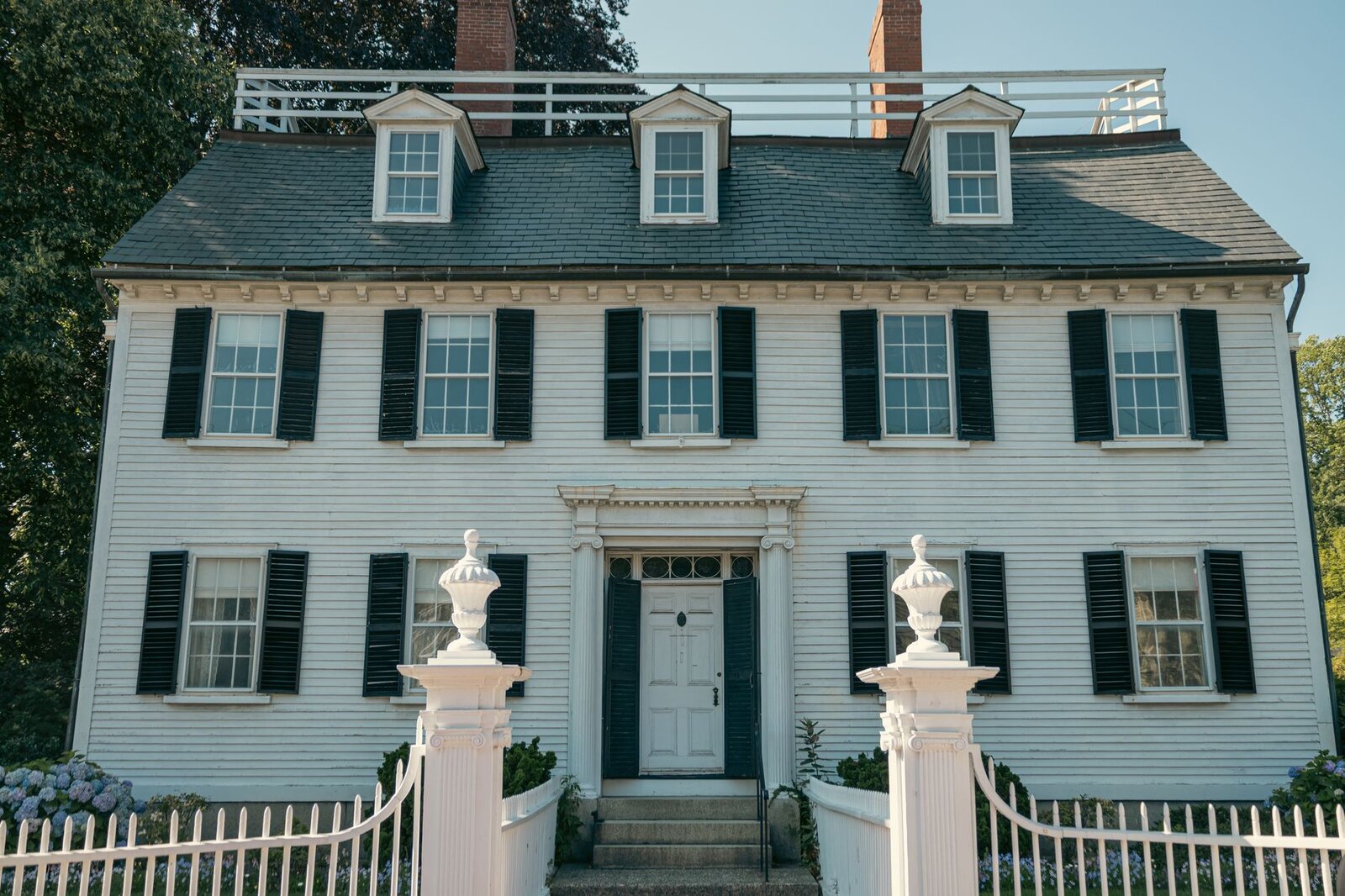 White clapboard New England colonial home with an added dormer and black shutters